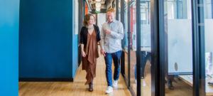 Woman and man walking down a hall with wood floor