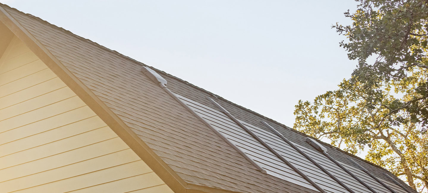 A sloped roof with solar panels is shown alongside a partially visible tree against a clear sky.